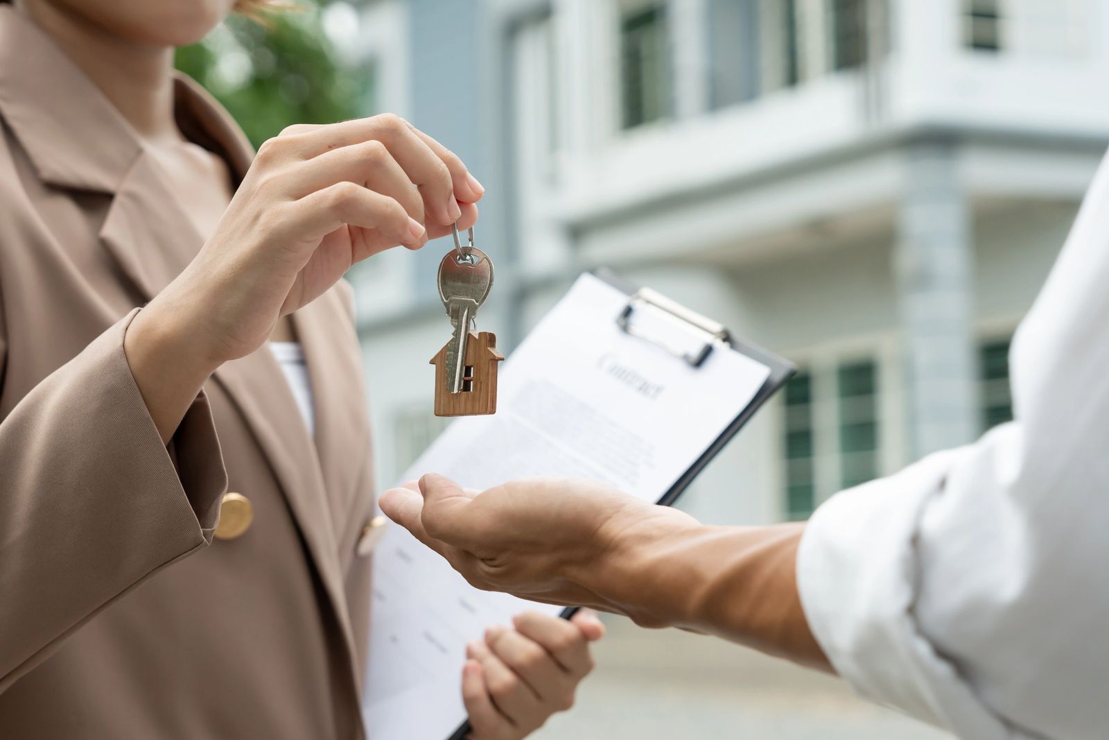 A real estate agent handing over a house key to a new tenant while holding a contract on a clipboard