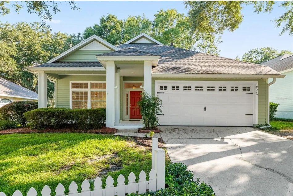 A green craftsman-style bungalow in Gainesville, Florida with a white picket fence and a red front door, one of the properties listed on GNV Bitcoin BnB